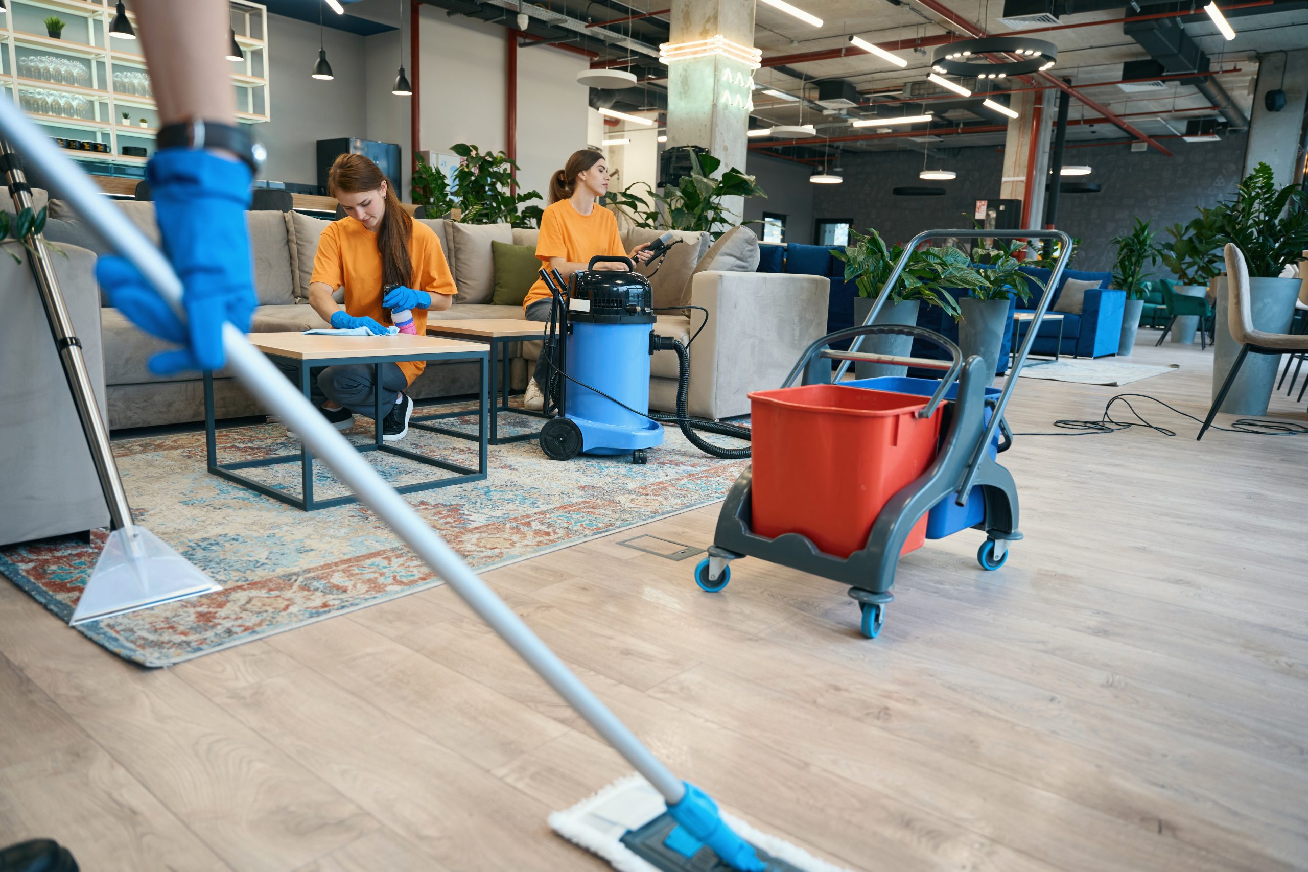 Cleaning in the coworking area, workers use a vacuum cleaner, mop, and buckets on a special cart